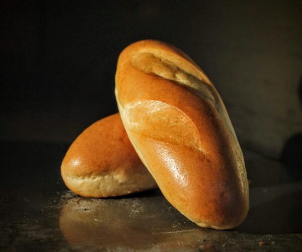 Two golden-brown rolls with a glossy crust rest on a dark surface.