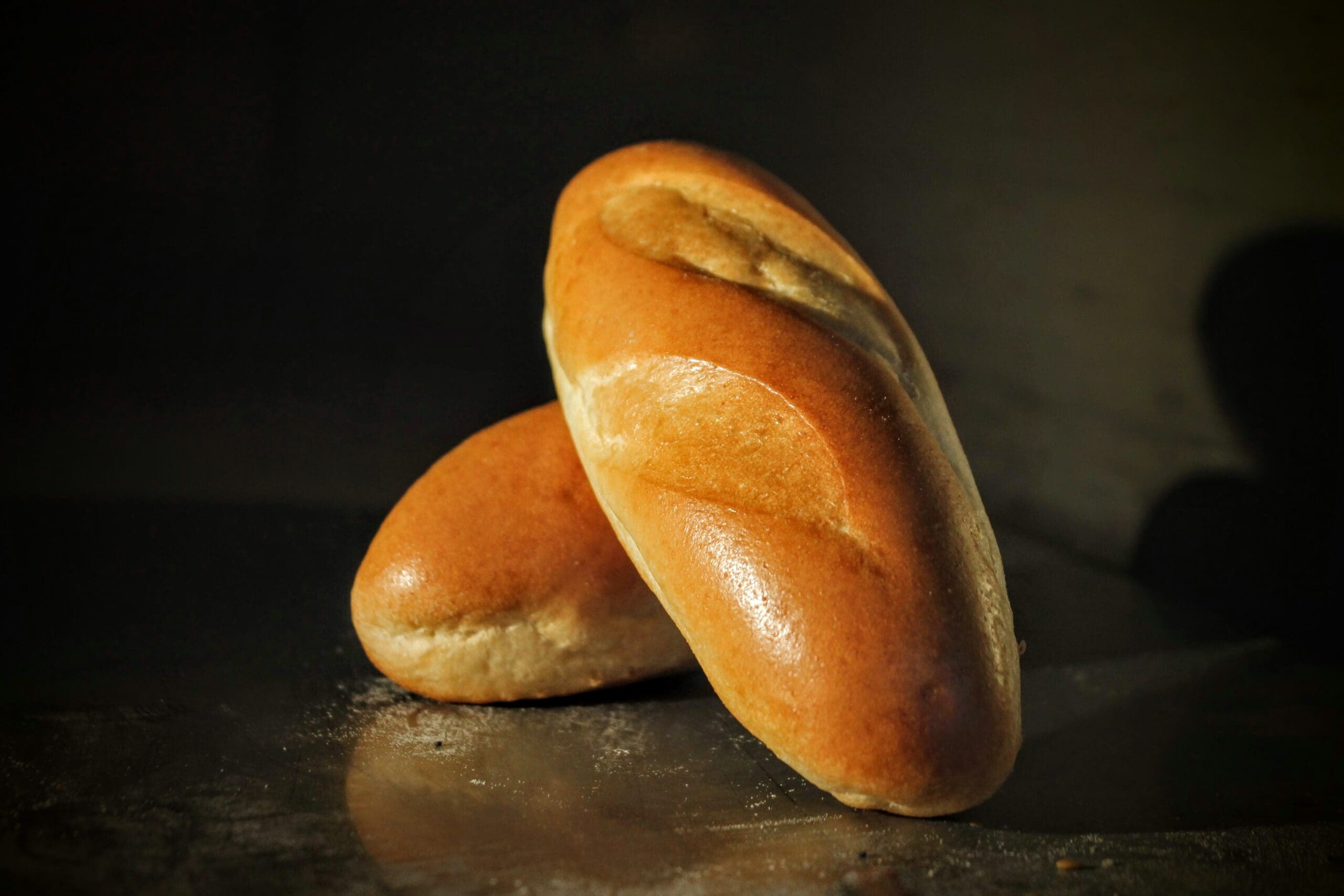 Two golden-brown rolls with a glossy crust rest on a dark surface.